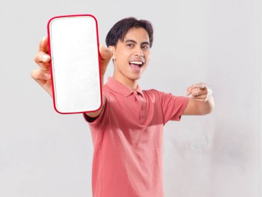 Heyecanlı Asyalı genç adam boş akıllı telefon ekran modelini tutuyor ve mobil uygulama promosyonu için sade arka planda izole ediyor.