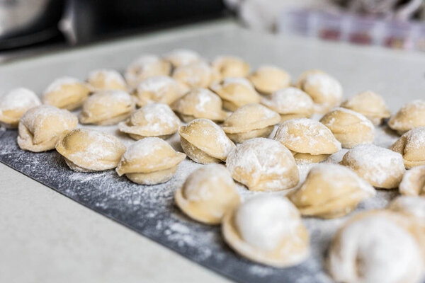 Raw homemade dumplings arranged on a floured board in the kitchen. Traditional cooking process before boiling. Close-up of uncooked pelmeni. High quality photo