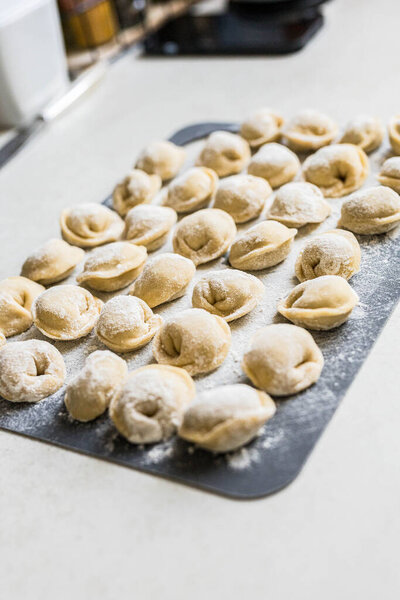 Raw homemade dumplings arranged on a floured board in the kitchen. Traditional cooking process before boiling. Close-up of uncooked pelmeni. High quality photo