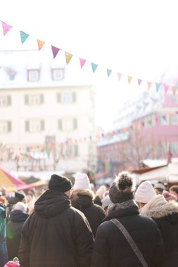 Stuttgart, Almanya... 18 Aralık 2022, sıcak kış kıyafetleri içinde renkli bayraklar ve tatil atmosferiyle süslenmiş parlak ve şenlikli bir Noel pazarında yürüyen bir kalabalık. Yüksek kalite fotoğraf