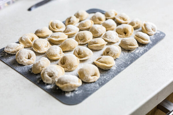 Raw homemade dumplings arranged on a floured board in the kitchen. Traditional cooking process before boiling. Close-up of uncooked pelmeni. High quality photo