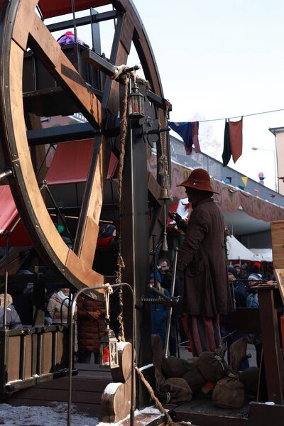 Vintage-style wooden Ferris wheel operated manually by a man in historical costume at a festive Christmas market. Family fun and tradition. High quality photo