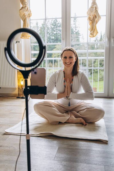 Woman practicing kundalini yoga and teaching an online class from home sitting in lotus position in front of camera during meditation session promoting balance and mental health. High quality photo
