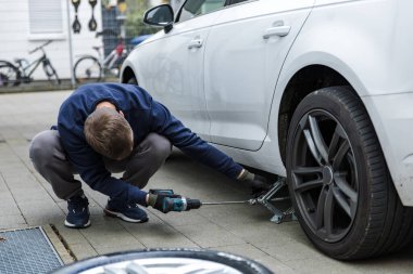 Genç bir adam yolda lastiği patlak bir şekilde değiştirirken bir ingiliz anahtarıyla vidaları söküyor. Yüksek kalite fotoğraf