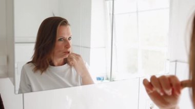 Parlak banyoda dişlerini fırçalayan bir kadın. Sabah rutini, diş bakımı, hijyen, tazelik, sağlık, kişisel bakım, doğal güzellik, ağız temizliği, sağlıklı yaşam tarzı, günlük ritüel, sağlık. Yüksek kaliteli FullHD görüntüler