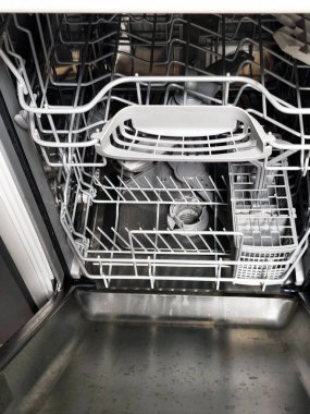 Temiz turkuaz bardaklar ve tabaklar düzgünce yerleştirilmiş bulaşık makinesini aç. Modern mutfak gereçleri paslanmaz çelik ve organize bulaşık raflarıyla donatılmış..