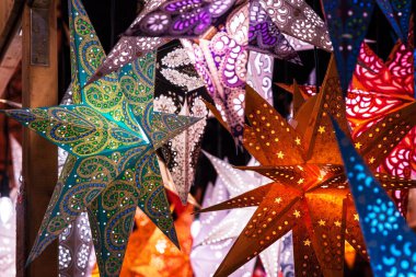 Dekoratif yıldız şeklindeki fenerler canlı renkler ve desenler Noel pazarında bir bayram tezgahında asılı duruyor.,