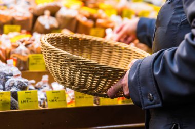 Boş bir hasır sepeti tutarken sıra sıra baharat arayan bir müşterinin elleri. Yavaş alışveriş, mevsimlik piyasa ve sıfır atık yaşam tarzını temsil ediyor.