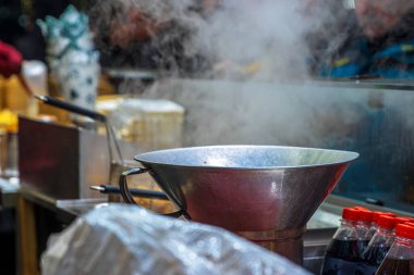Bir metal tencere ve fritöz tezgahın üzerine yerleştirilmiş şişeler ve ambalaj malzemeleriyle birlikte bir Noel marketinin açık mutfağına buhar salıyor..