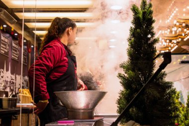 Wuerzburg, Almanya, 22 Aralık 2024. Üniformalı bir satıcı buharda pişen metal bir tencerenin arkasında sosis ve fransız freis tezgahında yemek pişiriyor.