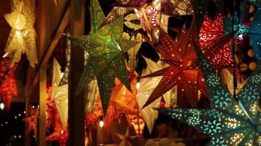 Wuerzburg, Almanya, 20 Aralık 2024. Ziyaretçi canlı kırmızı, turuncu, yeşil, mavi ışık saçan yıldız fenerlerinin altında duruyor. Şenlikli bir Noel Pazar akşamının samimi büyüsü.