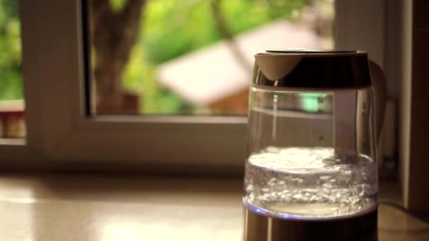 Een transparante theepot met water kookt en creëert grote bellen tegen een zonsondergang die door een raam schijnt. Het concept van een koffiepauze en het einde van de dag. Warme zomeravond ontspannen. — Stockvideo