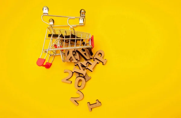 Feliz Año Nuevo 2021 se acerca. Las letras de madera cayeron de un carro de la compra sobre un fondo amarillo. Decoración festiva o concepto de postal. Vista superior y plana. Copiar espacio —  Fotos de Stock