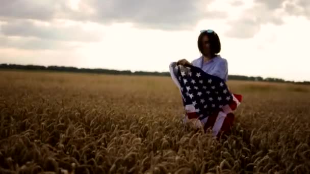 Un joven activista estadounidense con la bandera de Estados Unidos y camina en un campo de trigo al aire libre. Celebrando el Día de la Independencia. — Vídeos de Stock