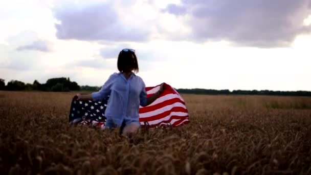 Молодой американский активист кружит вокруг флага США и ходит по пшеничному полю под открытым небом. Празднование Дня независимости. — стоковое видео