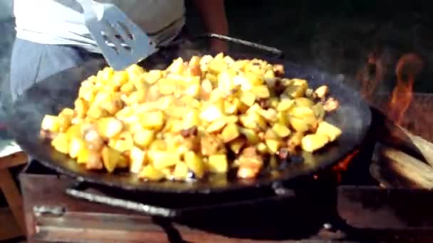女の子は彼らが焼かれないようにベーコンでジャガイモを裏返します。火の上にラードで揚げジャガイモを調理します。焼き芋料理. — ストック動画