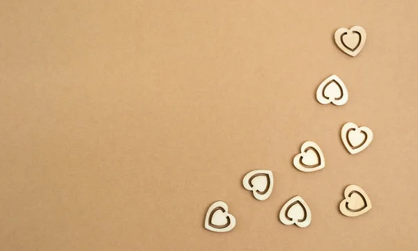 Corazones de madera sobre un fondo de papel artesanal pastel. Fondo abstracto con formas cortadas en madera. San Valentín, día de las madres, tarjetas de felicitación de cumpleaños, invitaciones. Copiar espacio. — Foto de Stock