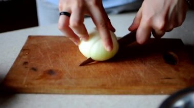 Kadın, salata için tahta bir tahtanın üzerinde keskin bir bıçakla soğanı ince ince doğruyor. Evde yemek pişirme kavramı.
