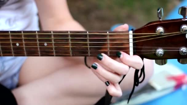 Kobieca ręka z manicure trzyma strunę gitary. Dziewczyna gra na gitarze w naturze. Koncepcja uczenia się grać na gitarze.Podstrunnica i progi. — Wideo stockowe