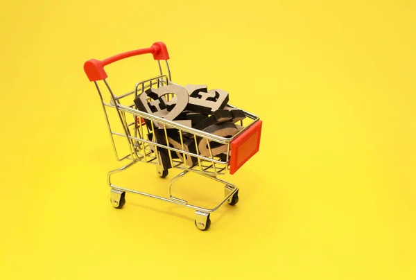 Letras de madera del alfabeto inglés se encuentran en un carrito de compras en miniatura sobre un fondo amarillo, primer plano.Concepto de compra de conocimiento. Copiar espacio. —  Fotos de Stock