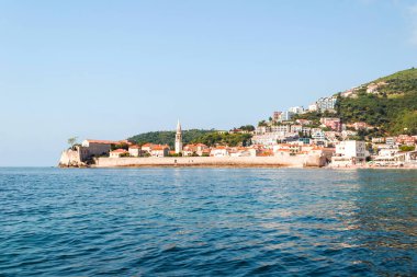 Deniz kıyısındaki bir körfezin yüksek açılı görüntüsü ve parlak güneşli bir günde arka planda dağ olan küçük bir kasaba. Perast, Karadağ 'ın eski bir kasabası
