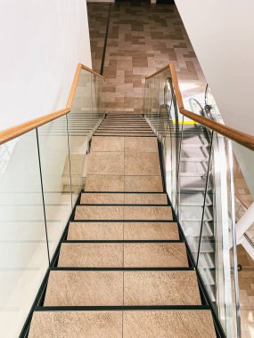 Parlak ahşap parmaklıklar ve şeffaf cam panellerden oluşan modern merdiven, güzel tasarlanmış fayanslı zemine iniyor, davetkar ve çağdaş bir atmosfer yaratıyor.