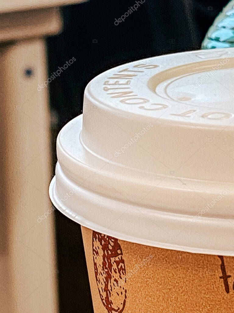 Detailed close-up of a disposable coffee cup with a textured lid, emphasizing branding and material quality in a casual setting