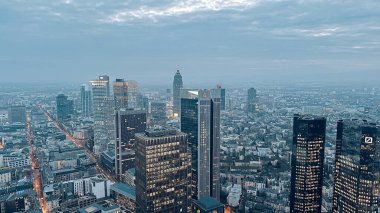 Günbatımında çekilen şehir silueti, aydınlık pencereli modern gökdelenleri gözler önüne seriyor, şehir ışıkları cam yüzeyleri yansıtıyor, metropol manzarasında canlı bir atmosfer yaratıyor.