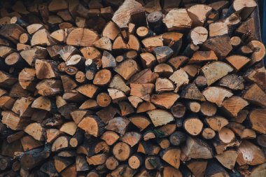 Yığınlanmış odun kütükleri, sade bir ortamda düzgün bir şekilde dizilmiş, odunların doğal dokusunu ve sıcak renklerini vurguluyor, açık hava ortamları için samimi ve davetkar bir atmosfer yaratıyor.