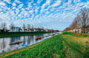 Güzel nehir manzarası, yemyeşil bankalar yansıtıcı su ve dinamik bulut desenleri, dinamik bir atmosfer yaratıyor.