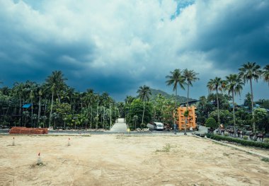 Pataya, Tayland - 1 Mayıs 2023 İnşaat Alanı, canlı palmiye ağaçları ve yeşilliklerle çevrili, bulutlu bir gökyüzü ile gelişmekte olan bir çevreyi gösteren kumlu bir araziye sahiptir.