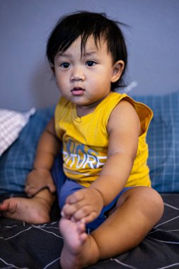 Yürümeye başlayan çocuk sessizce yatakta bekler, yatağında sessizce bekleyen bir bebeğin sakin bir reklam fotoğrafı, yumuşak ışıkta katlanmış minik eller, sakin çocuk kampanyası veya barışçıl sabır belgeseli için mükemmel..