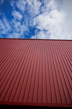 Parlak Mavi Gök 'e Karşı Kırmızı Konteynır, yoğun güneş ışığı altında, lojistik güç veya endüstriyel belgesel için keskin duran kırmızı konteynır..