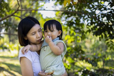 Anne Tutucu Çocuk Izgara Domuz Bahçesi Sabahı, sıcak ve otantik bir fotoğraf, çocuğunu kucaklayan bir anne açık havada ızgara domuz eti yerken, yemek reklamları ve aile belgeseli için.