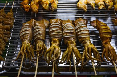 Izgarada marine edilmiş mürekkep balığı şişleri, marine edilmiş mürekkep balığının cızırtılı fotoğrafı, parlak dokunaçlar ve ızgarada marine edilmiş salamura ile parlayan kömürleşmiş kenarlar, deniz ürünleri barbeküsü ya da sokak yemekleri belgeseli için..