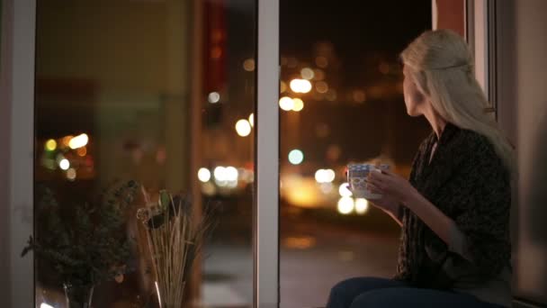 Pencere kenarında oturan, sıcak çay içme ve sokağa bakan kız — Stok video