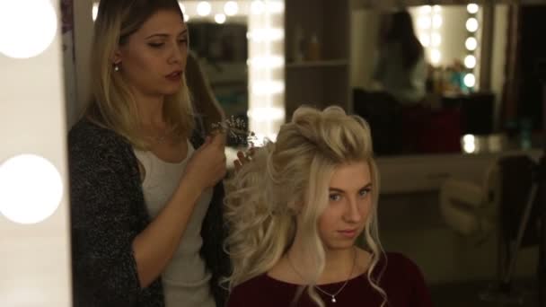 Um cabeleireiro profissional faz o penteado da menina, menina loira — Vídeo de Stock