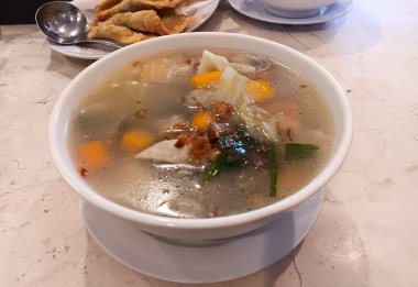 Endonezya Çin yemeği, sebzeli berrak tavuk çorbası: havuç, lahana, mantar, patates, domates üzerine kızarmış arpacık soğanı, mermer masada izole edilmiş beyaz bir kase..