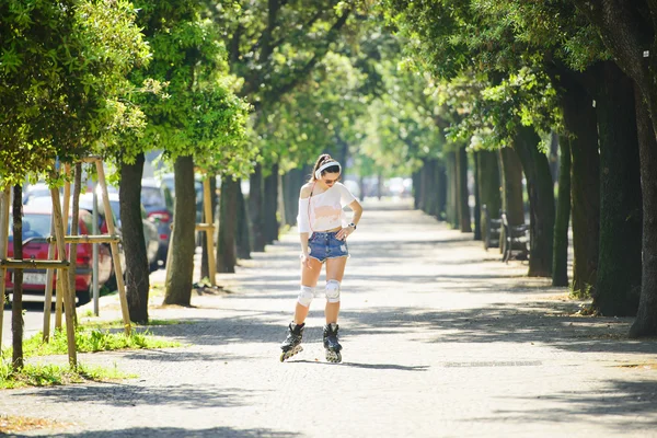 Tekerlekli paten parkta sürme ve bir cep telefonu kullanarak genç atlet kısa denim şort.