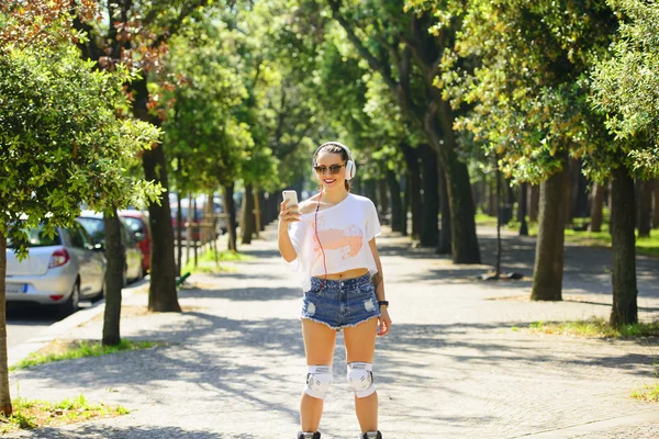 Tekerlekli paten parkta sürme ve bir cep telefonu kullanarak genç atlet kısa denim şort.