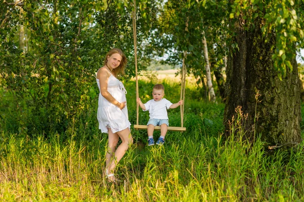 Pregnant mom with a boy resting in a meadow. — Stock Photo, Image