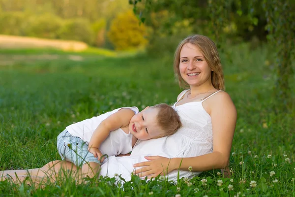 Těhotné Máma s klukem odpočívá na louce. — Stock fotografie