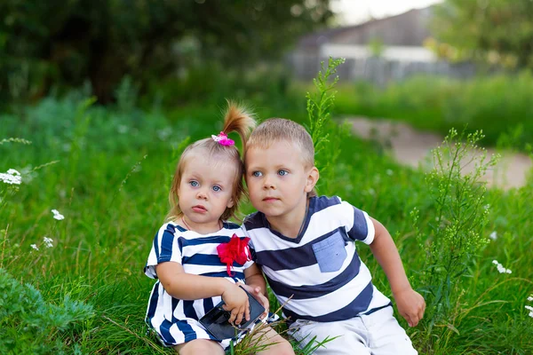 Liten pojke och flicka med kameran sitter på gräset utomhus — Stockfoto