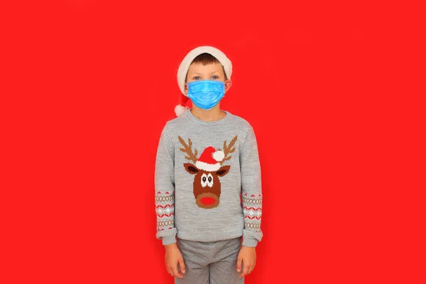 Αγόρι που φοράει αναπνευστική μάσκα και πουλόβερ της Πρωτοχρονιάς σε κόκκινο φόντο. — Φωτογραφία Αρχείου