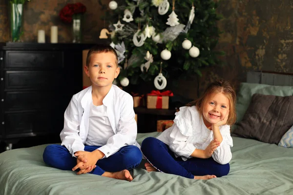 As crianças estão sentadas na cama em frente à árvore de Natal. — Fotografia de Stock