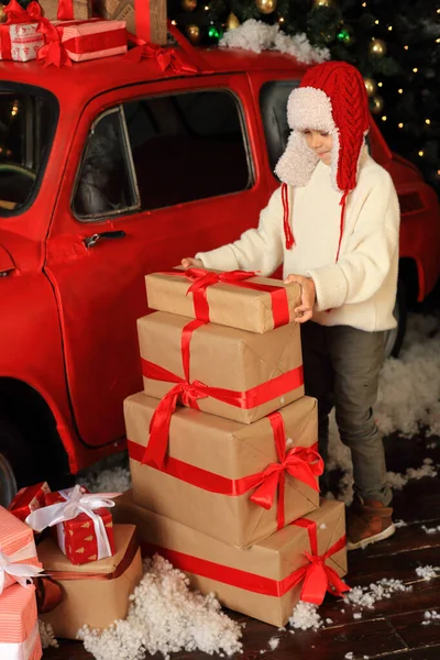 Menino no fundo de um carro vermelho com presentes. — Fotografia de Stock