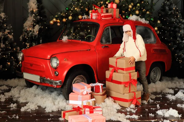 Menino no fundo de um carro vermelho com presentes. — Fotografia de Stock