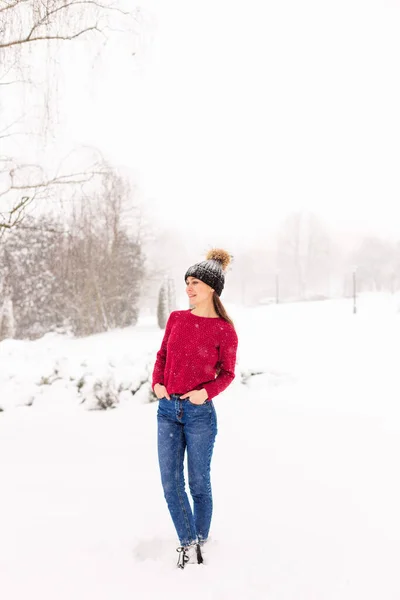 Girl in red in a snowy park in winter when it snows. — Stock Photo, Image