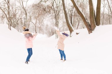 İki kız ormanda kışın kartopu oynuyor..