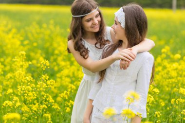 Çiçek açan kolza tohumu tarlasında iki kız yürüyor..